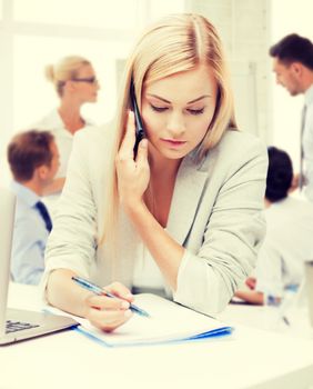 business concept - businesswoman talking on the phone and taking notes in office