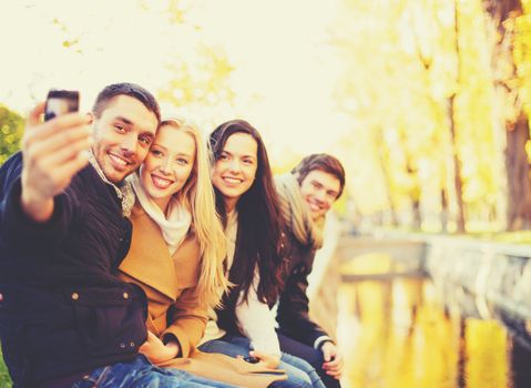 holidays, vacation, travel and tourism concept - group of friends or couples having fun in autumn park and taking selfie