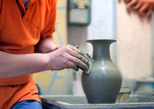 On a rotating pottery wheel wizard manually manufactures ceramic vase.