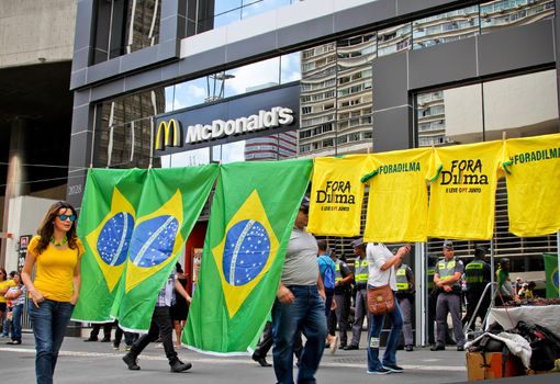 SAO PAULO, BRAZIL August 16, 2015: An unidentified woman walks in front of a flag vendor in the protest against federal government corruption in Sao Paulo Brazil. Protesters call for the impeachment of President Dilma Rousseff.