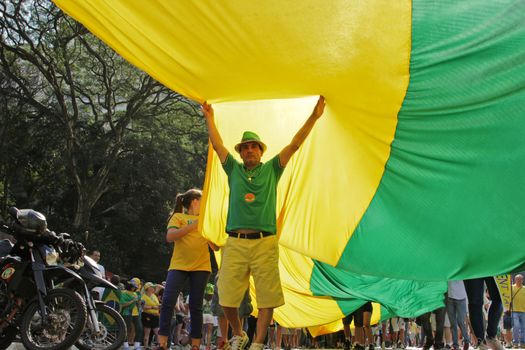 SAO PAULO, BRAZIL August 16 2015: An unidentified man below of a big flag in the protest against federal government corruption in Sao Paulo Brazil. Protesters call for the impeachment of President Dilma Rousseff.