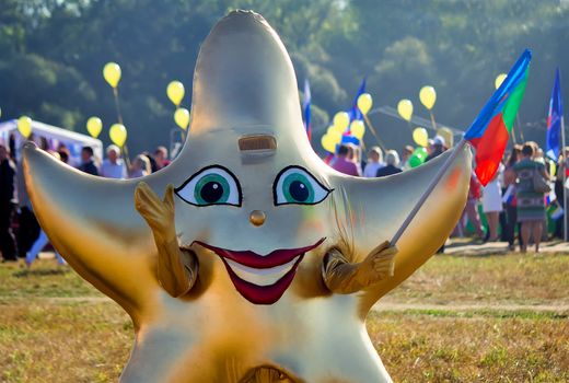 Depicts a man in a funny costume in the form of a star with a flag in his hand at the festival.