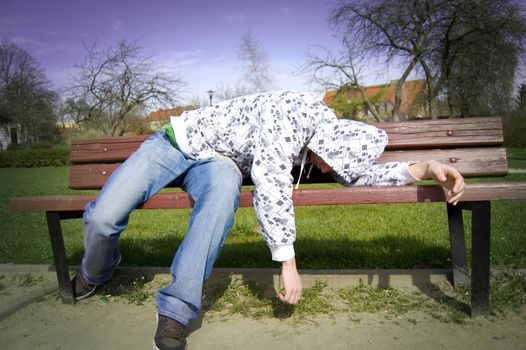 A drunken man lying on a park bench.