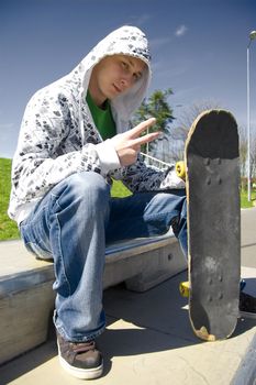 Skateboarder conceptual image. Skateboarder sits in skatepark and shows a youth gesture.
