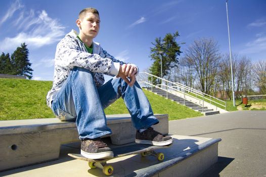 Skateboarder conceptual image. Teenage skateboarder sits in skatepark.