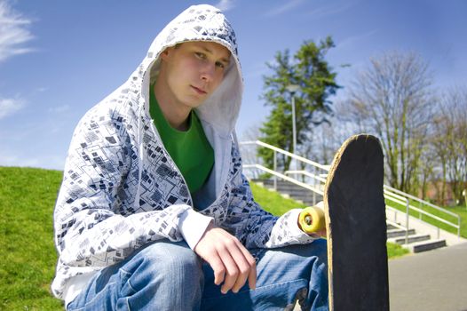 Teenage skateboarder conceptual image. Teenage skateboarder sits in skatepark.