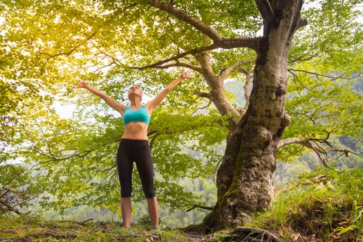 Active sporty girl raising arms inhaling fresh air, feeling  relaxed and free in beautiful natural environment. . Concept of natural, active, healthy, lifestile.