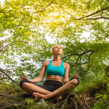 Relaxed woman enjoying freedom and life in beautiful natural environment. Blissful girl in lotus pose feeling relaxed, free and happy. Concept of freedom, happiness, enjoyment and natural balance.