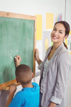 Portrait of pretty teacher helping pupil at chalkboard in a classroom