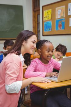 Happy teacher using laptop with student at the elementary school