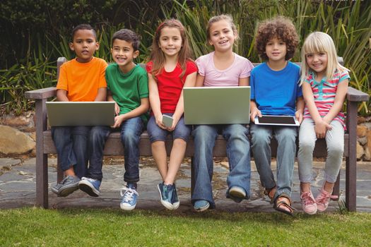 Kids sitting on a park bench with laptops