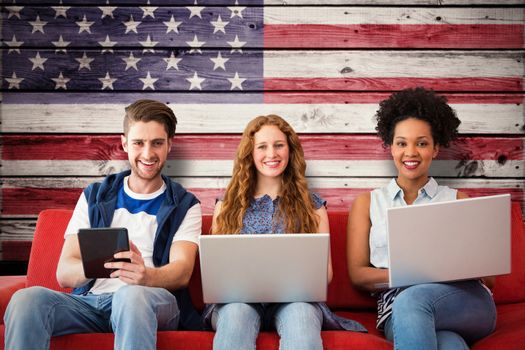 Young adults using electronic devices on couch  against composite image of usa national flag