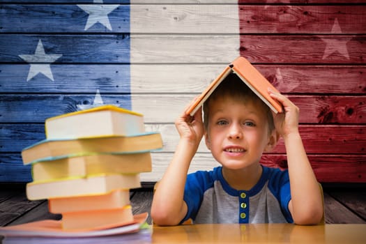 Cute boy with book on head against composite image of usa national flag