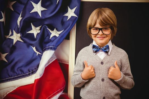 Cute pupil dressed up as teacher against american flag on chalkboard