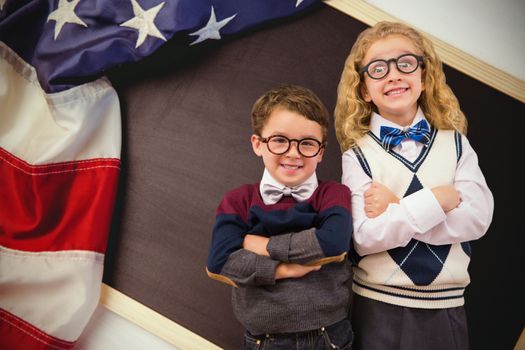 Cute pupils looking at camera against american flag on chalkboard