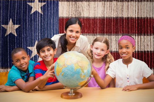 Cute pupils and teacher looking at globe in library  against composite image of usa national flag