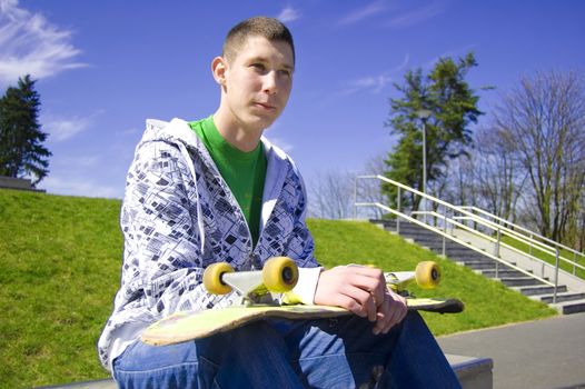 Teenage skateboarder conceptual image. Teenage skateboarder sits in skatepark.