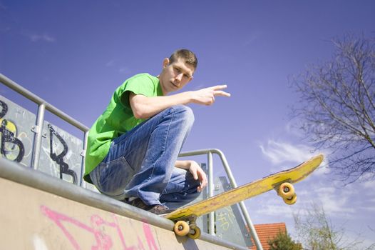 Sport conceptual image. Teenage skateboarder standing on the ramp with skateboard and shows a youth gesture.