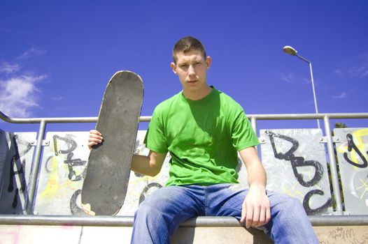 Teenage skateboarder conceptual image. Teenage skateboarder sits in skate-park.