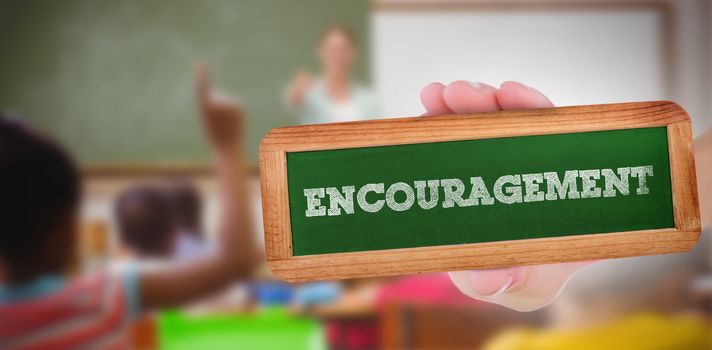 The word encouragement and hand showing chalkboard against pupils raising their hands during class