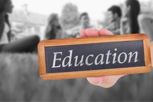 The word education and hand showing chalkboard against happy students sitting outside on campus 