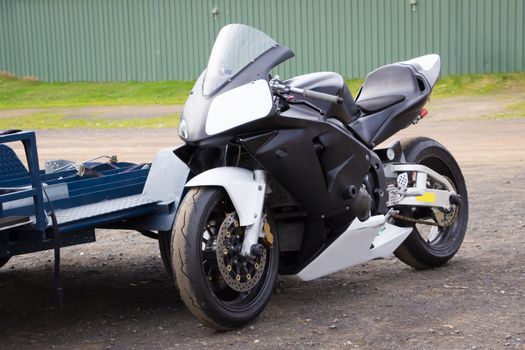 A modern racing superbike leaning against its trailer in the paddock at a racetrack.