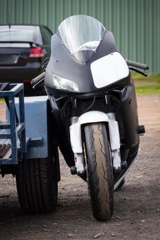 A modern racing superbike leaning against its trailer in the paddock at a racetrack.