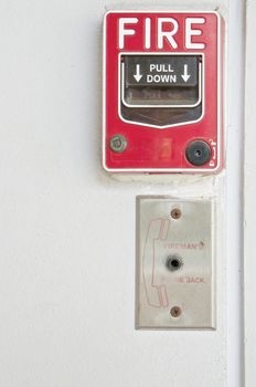Old red box of fire alarm on right with white wall background.