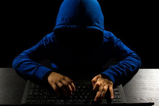 Faceless hacker with laptop in black isolated background.