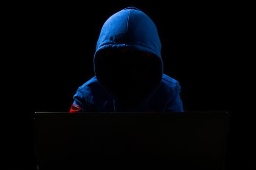 Faceless hacker with laptop in black isolated background.