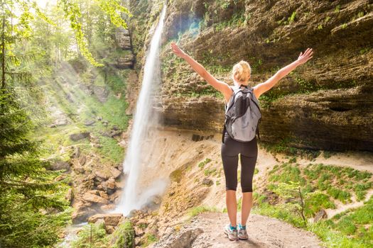 Female hiker raising arms inhaling fresh air, feeling relaxed and free in beautiful natural environment under Pericnik waterfall in Vrata Valley in Triglav National Park in Julian Alps, Slovenia.