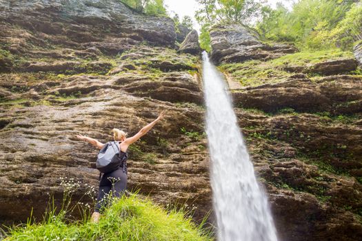 Female hiker raising arms inhaling fresh air, feeling relaxed and free in beautiful natural environment under Pericnik waterfall in Vrata Valley in Triglav National Park in Julian Alps, Slovenia.