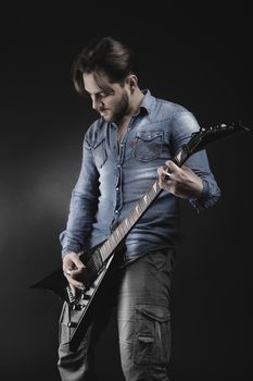 Handsome guitarist playing his electric guitar on black background