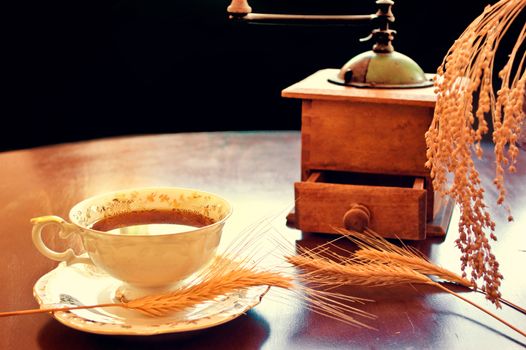 Coffee in antique porcelain cup on the table and old coffee grinder mill. Vintage instagram picture.