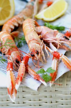 Delicious Grilled Langoustines with Lemon and Parsley on Newspaper closeup on Wicker background. Focus on Animal Eyes