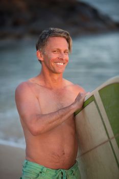 Smiling single adult Caucasian male at beach with surfboard