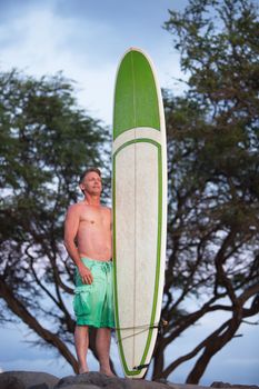 Proud athletic Caucasian adult male posing with surfboard outdoors
