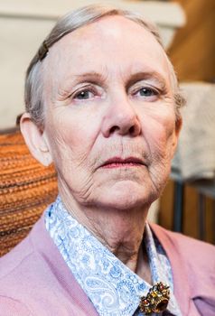 Stern elderly lady in pink sweater looking down at camera