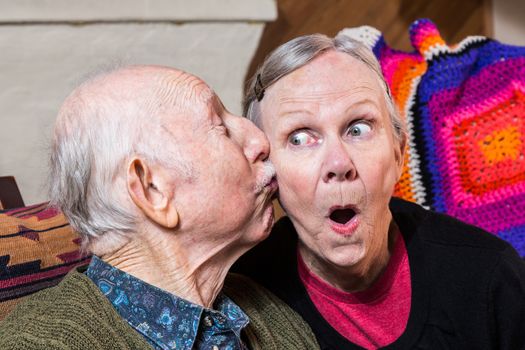 Elderly gentleman kissing elderly woman on cheek in livingroom