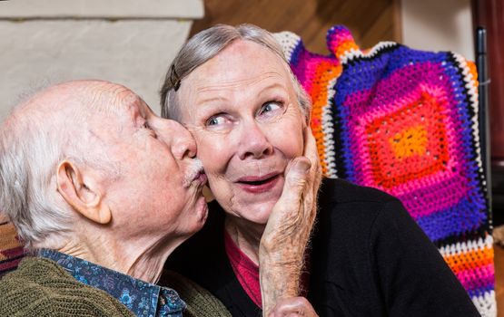 Elderly gentleman kissing woman on cheek in indoors