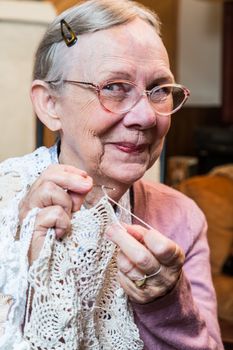 Elderly woman in pink sweater crocheting with demure smile