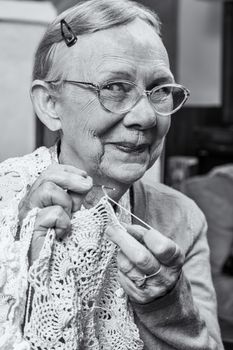Elderly woman in sweater crocheting with demure smile