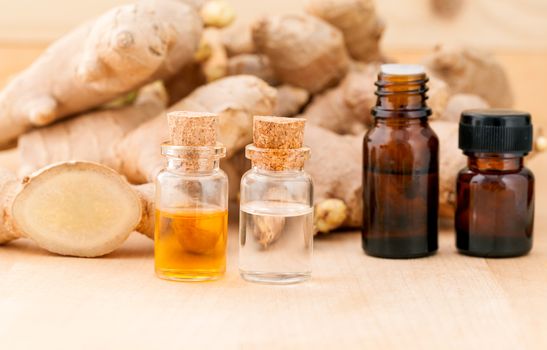 Bottles of ginger oil and ginger on wooden background with selective focus.