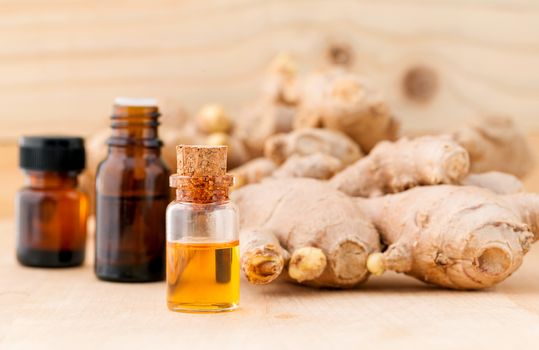 Bottles of ginger oil and ginger on wooden background with selective focus.