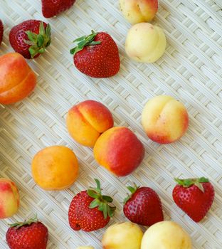 Arrangement of Fresh Ripe Apricots, Strawberries and Peaches closeup on White Wicker background. Top View