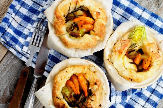 Delicious Puff Pastry Snacks with Shrimps, Leek and Cheese Oven-Baked in Ramekin on Checkered Napkin with Fork and Knife. Top View