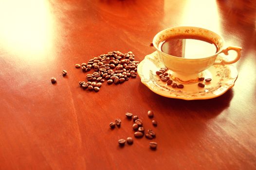 Coffee beans and hot coffee in the antique porcelain cup on the wooden table.