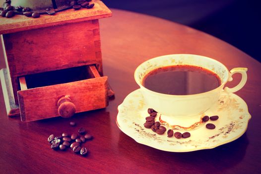 Coffee beans and cup of hot coffee and old coffee grinder mill. Vintage instagram picture. Antique porcelain cup