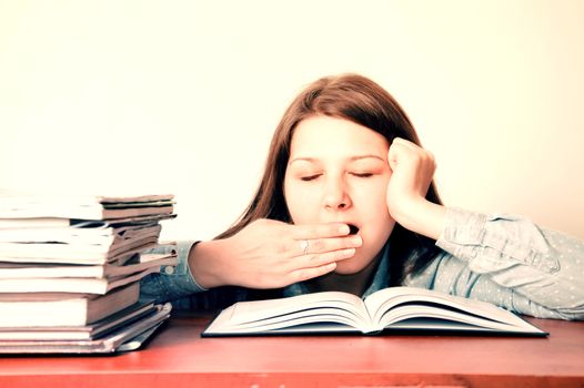 Education conceptual image. Young tired girl yawns during doing her homework.