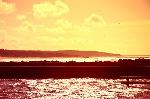 Coast and nature. Sunset over sea with jetty bathed in the sun rays.